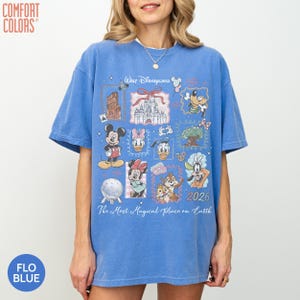 May include: A blue short-sleeve t-shirt featuring a graphic print of Walt Disneyland with various characters including Mickey Mouse, Minnie Mouse, Donald Duck, Daisy Duck, Goofy, Chip and Dale, and the text The Most Magical Place on Earth 2026.