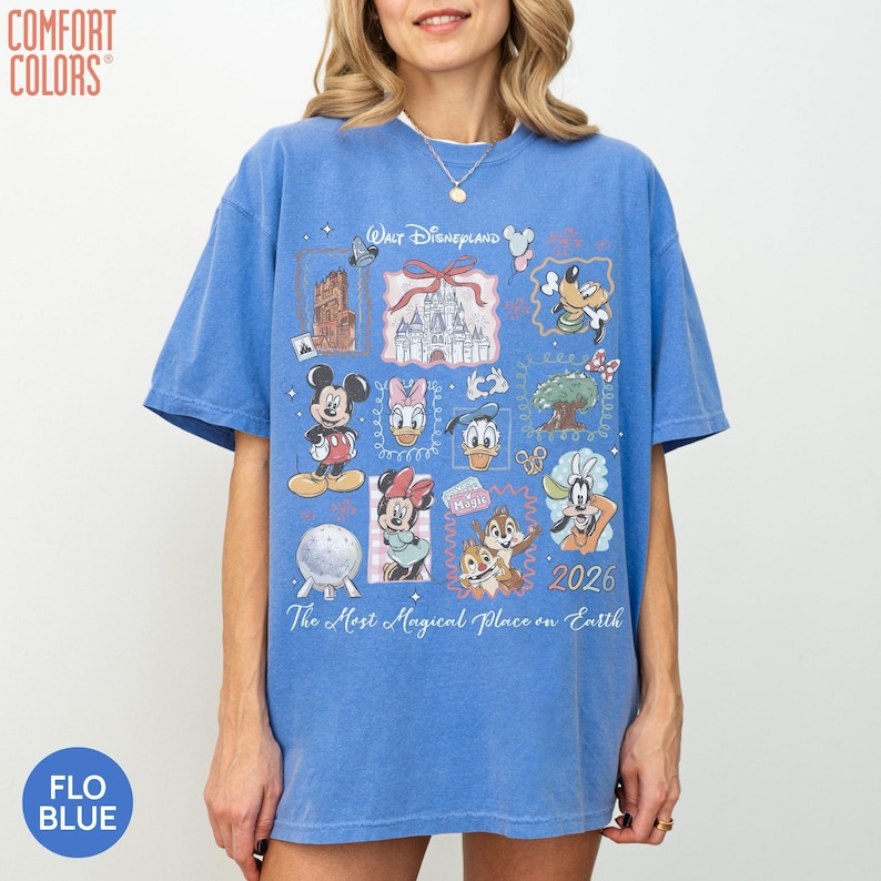 May include: A blue short-sleeve t-shirt featuring a graphic print of Walt Disneyland with various characters including Mickey Mouse, Minnie Mouse, Donald Duck, Daisy Duck, Goofy, Chip and Dale, and the text The Most Magical Place on Earth 2026.