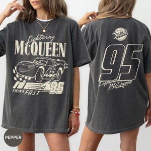 Pu&ograve; includere: T-shirt grigio scuro di Lightning McQueen. La parte anteriore presenta una grafica della macchina da corsa con la scritta "Lightning McQueen", "95" e "Think Fast". Il retro mostra un grande "95" e "Lightning McQueen" con il logo "Rusteze".