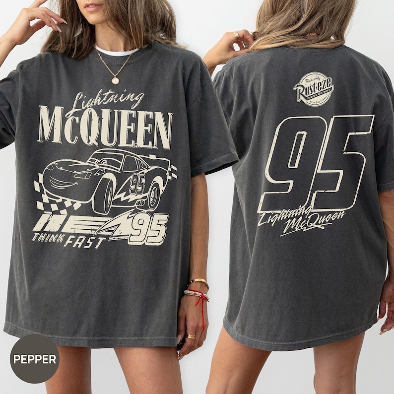 Pu&ograve; includere: T-shirt grigio scuro di Lightning McQueen. La parte anteriore presenta una grafica della macchina da corsa con la scritta "Lightning McQueen", "95" e "Think Fast". Il retro mostra un grande "95" e "Lightning McQueen" con il logo "Rusteze".