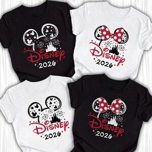 Puede incluir: Cuatro camisetas de manga corta en blanco y negro con un gr&aacute;fico de la silueta de la cabeza de Mickey o Minnie Mouse, un castillo, fuegos artificiales, estrellas y el texto Disney 2026. Dos camisetas incluyen un lazo rojo con lunares.
