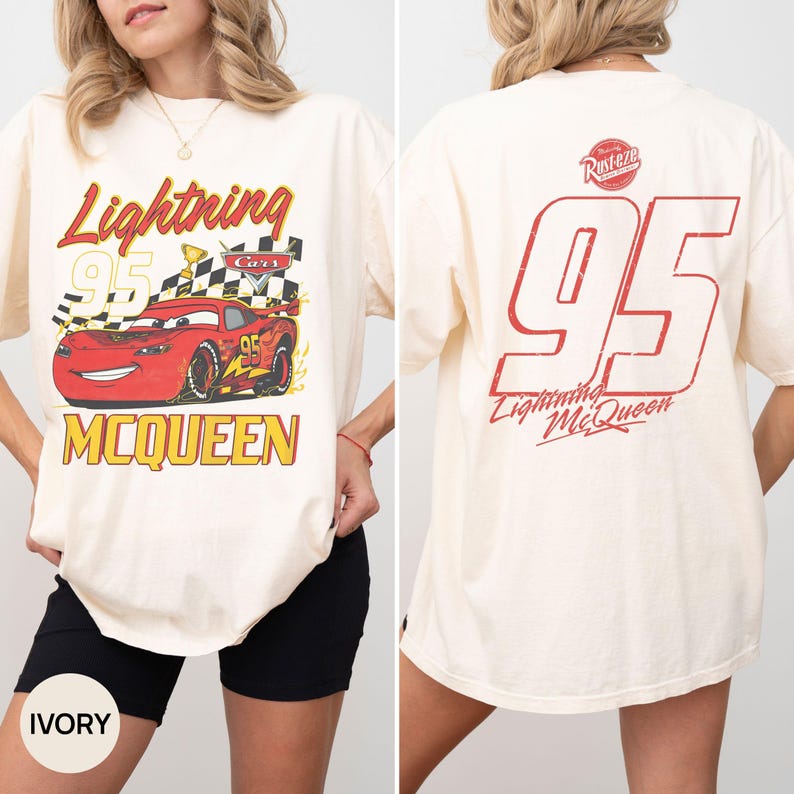 May include: Ivory-colored t-shirt featuring a graphic of Lightning McQueen from the Cars movie. The front design includes the text "Lightning 95 McQueen" with a checkered flag and a red race car. The back displays "95" and "Lightning McQueen".