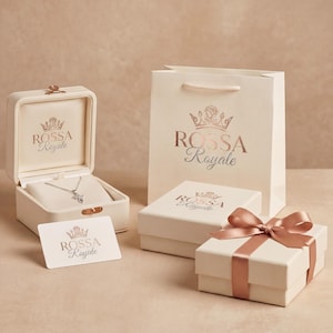 Pode incluir: Uma caixa de joias creme aberta com um colar de prata dentro, uma sacola de presente e duas caixas creme. As caixas e a sacola t&ecirc;m o texto "ROSSA Royale" impresso em ouro rosa. Uma caixa de presente &eacute; amarrada com uma fita de ouro rosa.