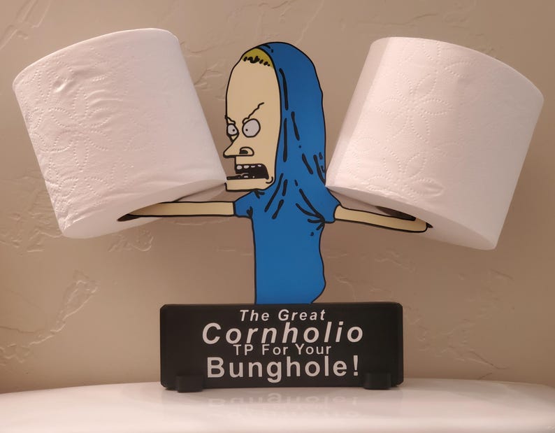May include: A novelty toilet paper holder featuring a cartoon character in a blue shirt and hood, holding two rolls of white toilet paper. The black base reads "The Great Cornholio TP For Your Bunghole!"