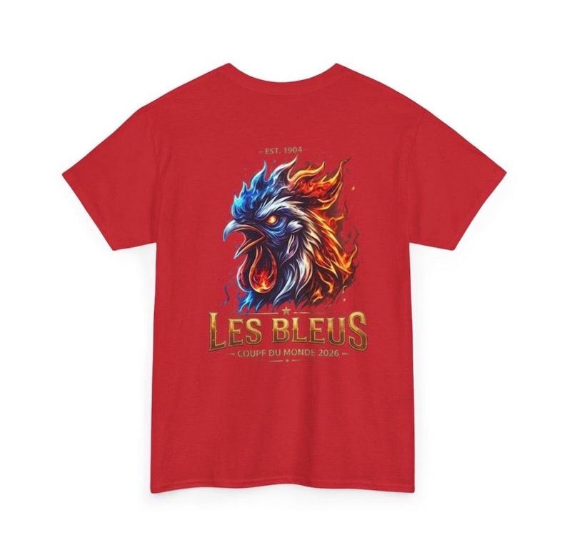 May include: Red t-shirt featuring a stylized rooster design with blue, orange, and white flames. The text "LES BLEUS - COUPE DU MONDE 2026" is displayed in gold lettering. The shirt also has the text "- EST. 1904 -" above the rooster.
