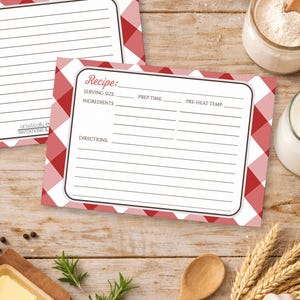 May include: Two recipe cards with a red and white gingham pattern. One card has lined spaces for writing, the other has spaces for serving size, ingredients, prep time, and directions. The cards are on a wooden surface.
