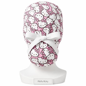 Könnte beinhalten: Eine rosa-weiß gemusterte OP-Haube mit dem Hello Kitty-Charakter. Die Haube hat eine weiße Schleife und Bindebänder. Sie wird auf einem weißen Schaufensterkopf mit dem Etikett "Hello Kitty" präsentiert.