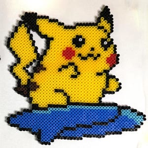 May include: Two pixel art figures made of yellow, black, red, and white plastic beads. One figure is a standing yellow creature with black-tipped ears and a lightning bolt tail. The second figure is the same creature sitting on a blue surfboard.