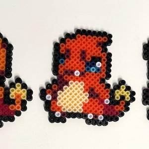 Könnte beinhalten: Drei Pixelkunstfiguren einer Charmander-Entwicklungslinie. Die Figuren bestehen aus bunten Plastikperlen. Die erste Figur ist orange, gelb und rot. Die zweite Figur ist rot und orange. Die dritte Figur ist orange, rot und schwarz.