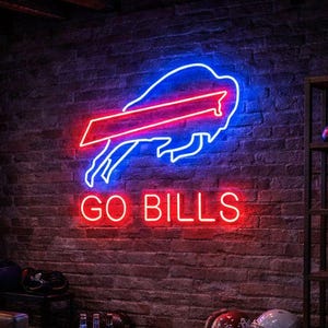 Könnte beinhalten: Ein Neonschild mit dem Logo der Buffalo Bills und dem Schriftzug "GO BILLS" in Rot und Blau. Das Schild befindet sich an einer Backsteinmauer in einem Raum mit Ledersesseln und einem Holztisch.