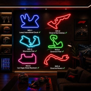 May include: Neon signs depicting six Formula 1 race circuits: Luseyl, Circuit of the Americas, Silverstone, Zandvoort, Las Vegas, and Monaco. Each sign glows in a different color against a dark wall. A Formula 1 car model and helmet are on a table.