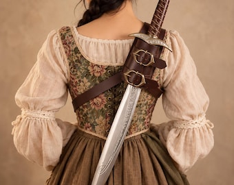 May include: A dagger with a silver blade featuring intricate engravings and a brown leather-wrapped hilt, secured in a brown leather scabbard with two brass buckles, worn over a floral patterned bodice with cream-colored long sleeves.