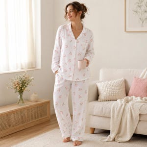 Peut inclure: Ensemble de pyjama blanc avec un motif de cerises roses. Le haut à manches longues a une fermeture boutonnée et un col cranté. Le pantalon assorti est ample. La personne tient une tasse rose. Le pyjama est en tissu doux et léger.