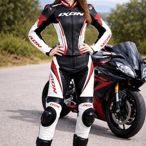 Puede incluir: Traje de moto de cuero negro, blanco y rojo con la marca "IXON" visible. El traje se lleva con botas negras y rodilleras. Una motocicleta negra y roja está en el fondo.
