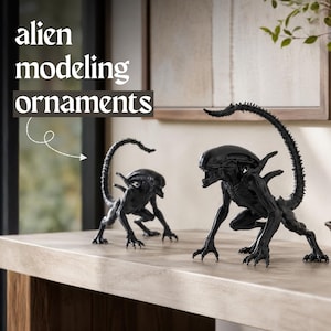 May include: Two black alien modeling ornaments are displayed on a light-colored surface. The ornaments are detailed sculptures of the iconic alien creature, with elongated heads, sharp claws, and long tails. The text "alien modeling ornaments" is in the upper left.