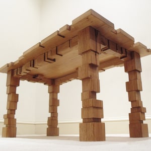 Puede incluir: Una mesa de madera con un diseño único. La superficie de la mesa está hecha de bloques de madera apilados, y las patas también están hechas de bloques apilados. La mesa está hecha de madera natural y tiene un aspecto rústico.