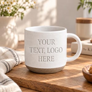 Peut inclure: Une tasse en céramique blanche avec une anse et une base grise. L'avant de la tasse présente le texte en relief "YOUR TEXT, LOGO HERE" dans une police serif. La tasse a une finition mate lisse et une forme cylindrique avec un bord inférieur arrondi.