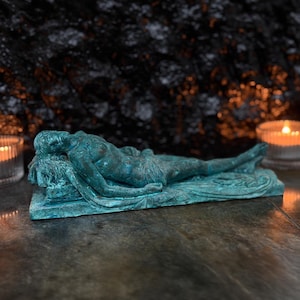 May include: A teal-colored sculpture of a reclining figure resting on a rectangular base. The figure is depicted in a horizontal, prone position with detailed textures and a weathered, oxidized finish, showcasing a classic artistic form.