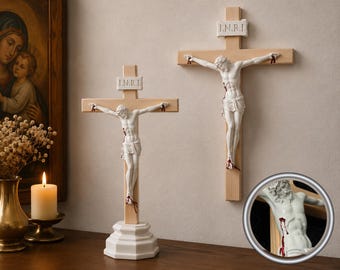 May include: Two crucifixes featuring light-colored wooden crosses and white figures of Jesus. Each figure has red painted details representing wounds and a white plaque at the top with the text I.N.R.I. One crucifix stands on a base, while the other is wall-mounted.