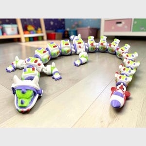 May include: A long, articulated toy dragon featuring a white, green, and purple color scheme inspired by a space ranger suit. The figure has a detailed head with a purple visor, multiple segmented body sections, and a pointed tail with red accents.