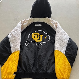 May include: A black, white, and yellow hooded jacket by Starter. The back features a large embroidered logo of a buffalo silhouette with the letters CU in yellow. The sleeves have quilted white panels on the shoulders and solid yellow cuffs.