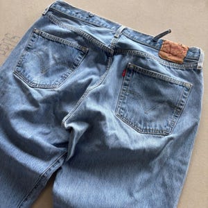 May include: Light blue denim jeans with classic five-pocket styling. The jeans feature the iconic Levi's brand label on the back and a red tab on the back pocket. The jeans are pre-worn and show signs of wear.