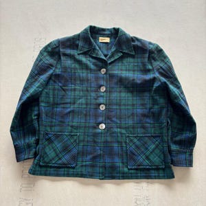 Könnte beinhalten: Grün-blaue karierte Jacke mit Kragen, vier Knöpfen und zwei Vordertaschen. Die Jacke hat ein klassisches Tartanmuster in Grün-, Blau- und Schwarztönen. Die Jacke ist mittelschwer und scheint aus einem gewebten Stoff zu sein.