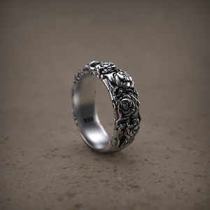 May include: A silver ring with a detailed floral design of roses. The ring is made of a shiny, metallic material and features a band covered in sculpted roses. The inside of the ring is stamped with the number "925".