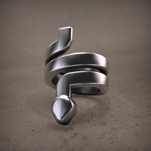 Op de afbeelding: Een zilverkleurige ring in de vorm van een opgerolde slang. De ring heeft een gladde, gepolijste afwerking en een gedetailleerde slangenkop. Het lichaam van de slang wikkelt zich om de vinger, wat een uniek ontwerp creëert. De achtergrond is neutraal.