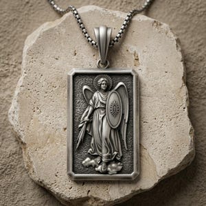 May include: A rectangular silver-toned pendant necklace featuring a relief of an angel holding a sword and a shield with a cross emblem. The pendant hangs from a silver box chain, showcasing a detailed metallic finish with dark oxidized accents.