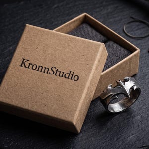 a brown cardboard box with the text "KronnStudio" printed on it, along with a silver ring placed inside the box.