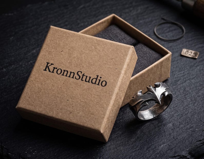 a brown cardboard box with the text "KronnStudio" printed on it, along with a silver ring placed inside the box.