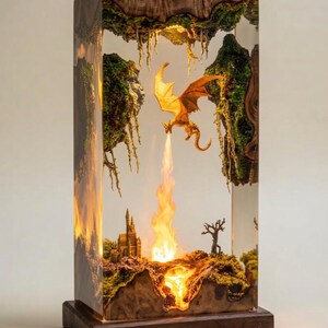 May include: A rectangular resin lamp featuring a wooden base and frame. Inside the clear resin, a miniature orange dragon flies above a small castle and a barren tree. The dragon breathes a stream of light, illuminating the scene from within.
