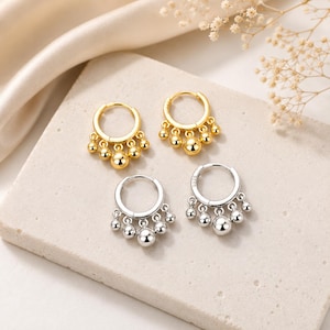 May include: Two pairs of hoop earrings, one gold-toned and one silver-toned. Each hoop features five dangling spherical beads of varying sizes, with the largest bead positioned in the centre. The silver earrings are clearly marked with S925.