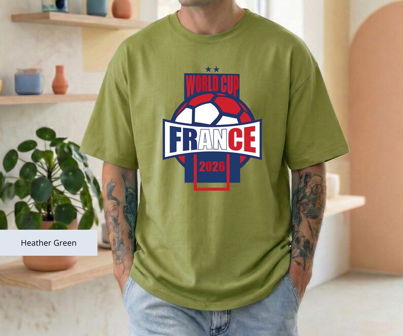 May include: A heather green short-sleeve t-shirt featuring a graphic of a soccer ball and the text "WORLD CUP FRANCE 2026" in red, white, and blue. The design is centered on the chest, showcasing a bold, athletic style with a round neckline.
