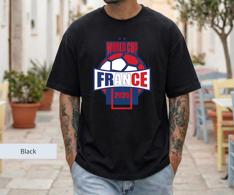 May include: A black short-sleeve t-shirt featuring a graphic design with a soccer ball and the text "WORLD CUP FRANCE 2026" in red, white, and blue colors. The design is centered on the chest and includes two small stars above the text.