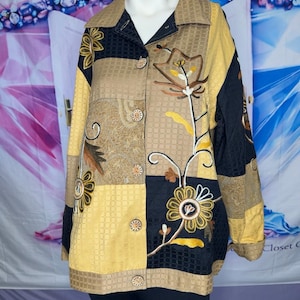 May include: A long-sleeve button-down shirt featuring a patchwork design in black, tan, and yellow. The garment displays a textured grid pattern and is decorated with embroidered floral motifs in white, yellow, and brown thread throughout the front.
