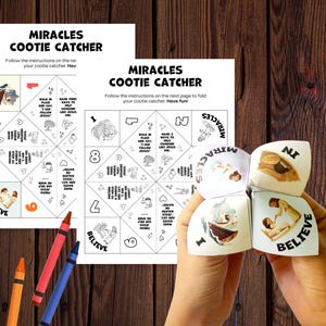 May include: A paper cootie catcher fortune teller featuring the text MIRACLES COOTIE CATCHER and religious illustrations. The game includes printed instructions, numbered sections, and prompts like BELIEVE. Two crayons are placed near the paper sheets.