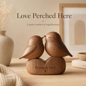May include: A wooden bird figurine featuring two birds perched on a base shaped like a heart. The base is engraved with the text "Emma & Noah" and a small heart symbol. The text "Love Perched Here" and "A quiet symbol of togetherness" appear above.