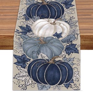 Peut inclure: Un chemin de table rectangulaire orné d'un motif répétitif de citrouilles dans des tons bleu marine foncé, bleu clair et blanc. Le design comprend des illustrations détaillées de feuilles d'automne et de vignes bleu marine et blanches sur fond beige.