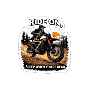 May include: A sticker featuring a skeleton riding an orange and black dirt bike. The skeleton wears a helmet and jacket. The text "RIDE ON, SLEEP WHEN YOU'RE DEAD" is above and below the image. The background includes trees and a setting sun.