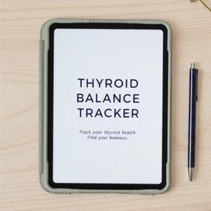 May include: A tablet with a gray case displaying the text "THYROID BALANCE TRACKER." The text "Track your thyroid health. Find your balance." is below the title. A blue pen with a gold tip rests beside the tablet on a light wood surface.