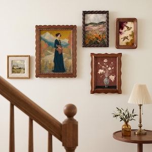 May include: A gallery wall arrangement featuring five framed artworks with wooden frames. The collection includes a painting of a person with sheep, a landscape with orange flowers, a bird illustration, a floral still life, and a small cottage scene.