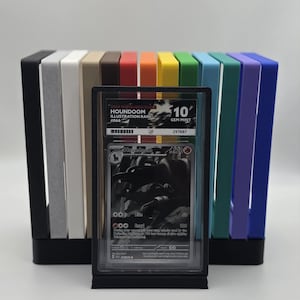 May include: A graded Houndoom illustration rare trading card, encased in a protective holder, with a Gem Mint 10 rating. The card is displayed in front of a colorful array of vertical card holders in various colors.