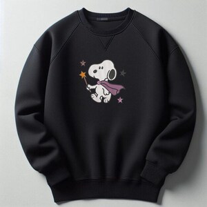 May include: A black long-sleeve sweatshirt featuring a graphic of a white cartoon dog wearing a purple cape and holding a yellow star-tipped wand. The design includes small pink and grey star accents surrounding the character on the chest area.