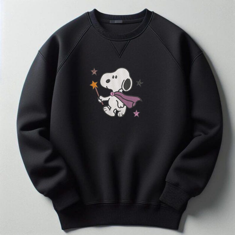 May include: A black long-sleeve sweatshirt featuring a graphic of a white cartoon dog wearing a purple cape and holding a yellow star-tipped wand. The design includes small pink and grey star accents surrounding the character on the chest area.