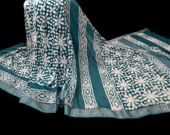 May include: Teal fabric with a white floral pattern and geometric border. The fabric is draped, showcasing the design. The floral pattern is a repeating design of white flowers. The border features a geometric pattern.