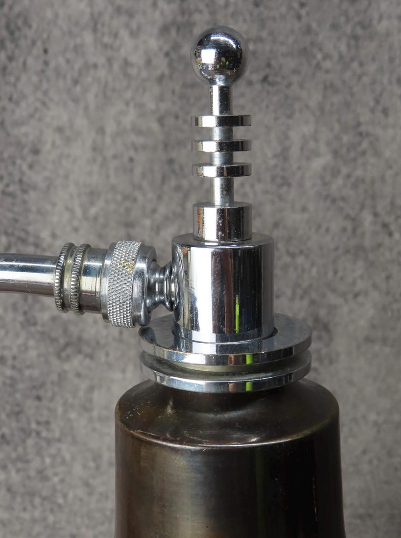 Puede incluir: Primer plano de un objeto met&aacute;lico cromado con una parte superior esf&eacute;rica y anillos apilados. Tiene una base cil&iacute;ndrica y un brazo curvo y texturizado. El art&iacute;culo es probablemente decorativo o funcional, posiblemente un grifo.