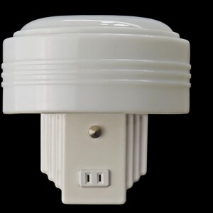 Puede incluir: Luz de noche blanca de estilo Art D&eacute;co, con una parte superior redondeada y una base rectangular. Incorpora una toma de corriente integrada y un peque&ntilde;o interruptor. El dise&ntilde;o presenta l&iacute;neas horizontales y detalles escalonados, creando una apariencia cl&aacute;sica y estilizada.