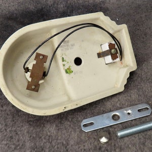 Puede incluir: Aplique de pared de cer&aacute;mica blanquecina con cableado negro y componentes met&aacute;licos. Incluye un soporte de montaje, una varilla roscada y una tapa decorativa. El aplique tiene forma ovalada curvada con borde decorativo.